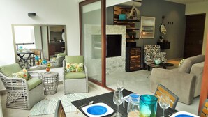 A modern living room with a dining area, featuring wicker furniture, a flat-screen TV, and a large mirror. - Amazing Tao loft overlooking the golf course. (Akumal)