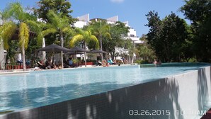 A swimming pool with lounge chairs and umbrellas, surrounded by trees and buildings. - Amazing Tao loft overlooking the golf course. (Akumal)