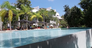 Ein Schwimmbecken mit Liegestühlen und Sonnenschirmen, umgeben von Bäumen und Gebäuden.