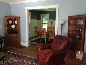 Cozy living room with a traditional design, featuring a leather armchair, sideboard, dining area, and patterned rug.