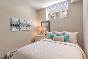 A bedroom with a bed, a nightstand, a lamp, and three wall-mounted paintings. - Tremblant Prestige - Clairiere 404 (Mont-Tremblant)