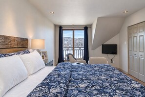 Une chambre d’hôtel comprenant un lit, un bureau, une chaise, une télévision et un balcon avec vue sur les montagnes.