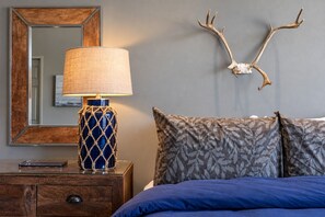 Ein Schlafzimmer mit einem Bett, einem Nachttisch mit Lampe, einem Spiegel und einer Wanddekoration aus Hirschgeweihen.