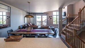 A spacious living area with a large dining table, comfortable seating, and a view of the outdoors. - Tremblant Prestige - Clairiere 404 (Mont-Tremblant)