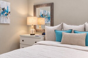 Une chambre à coucher avec un lit, une table de chevet avec une lampe, un miroir et des œuvres d’art accrochées au mur.