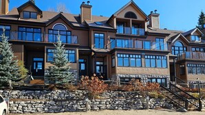 A multi-story house with a stone foundation, large windows, and a prominent chimney. - Tremblant Prestige - Clairiere 404 (Mont-Tremblant)
