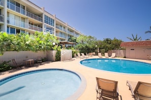 A hotel with a swimming pool, lounge chairs, and a building with balconies.