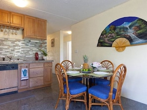 Una cocina con armarios de madera, salpicadero de azulejos y comedor con mesa para cuatro.