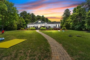 A house with a paved pathway leading to the entrance, surrounded by a well-maintained lawn and trees.