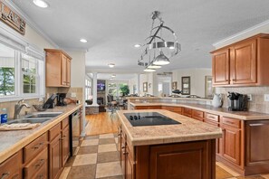 A spacious kitchen with wooden cabinets, granite countertops, and a central island with a stovetop.