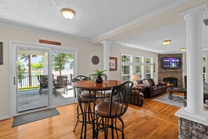 A spacious living room with a fireplace, a dining area with a round table, and a view of a lake through the sliding glass doors.