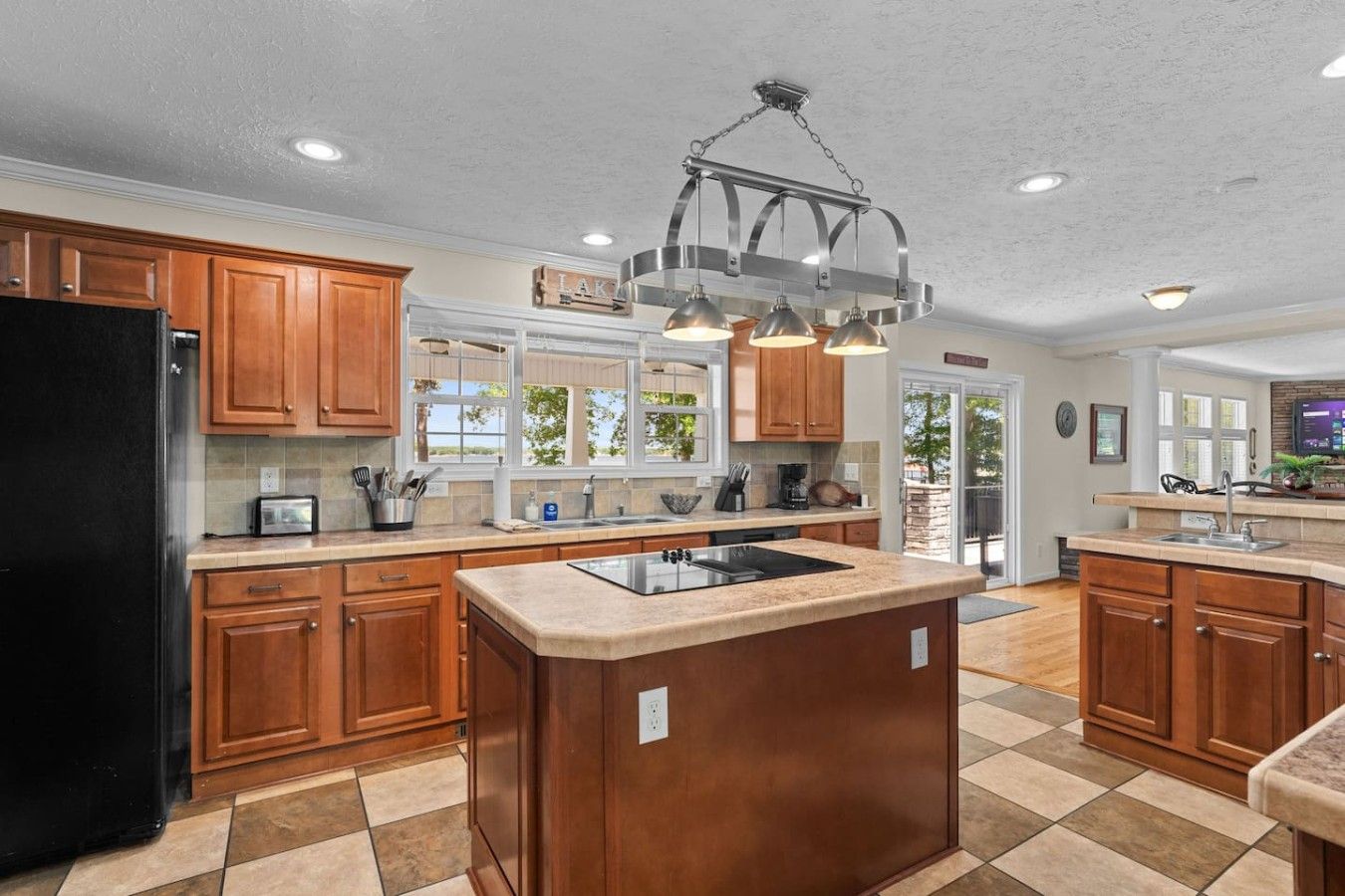 A kitchen with wooden cabinets, a black refrigerator, a central island with a sink, and pendant lighting.