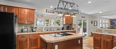 A kitchen with wooden cabinets, a black refrigerator, a central island with a sink, and pendant lighting.