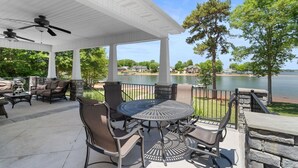 Une terrasse couverte, aménagée avec du mobilier d’extérieur, une table ronde et une vue sur un lac.