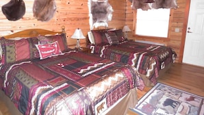 A log cabin room with two beds, a ceiling fan, and fur decorations on the walls.