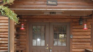 A wooden cabin with a brown door, a welcome sign, and a bench outside.