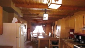 A wooden cabin interior with a kitchen area featuring a refrigerator, stove, and dining table with chairs.