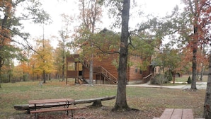 A rustic cabin with a staircase leading to a deck, surrounded by trees with autumn foliage.
