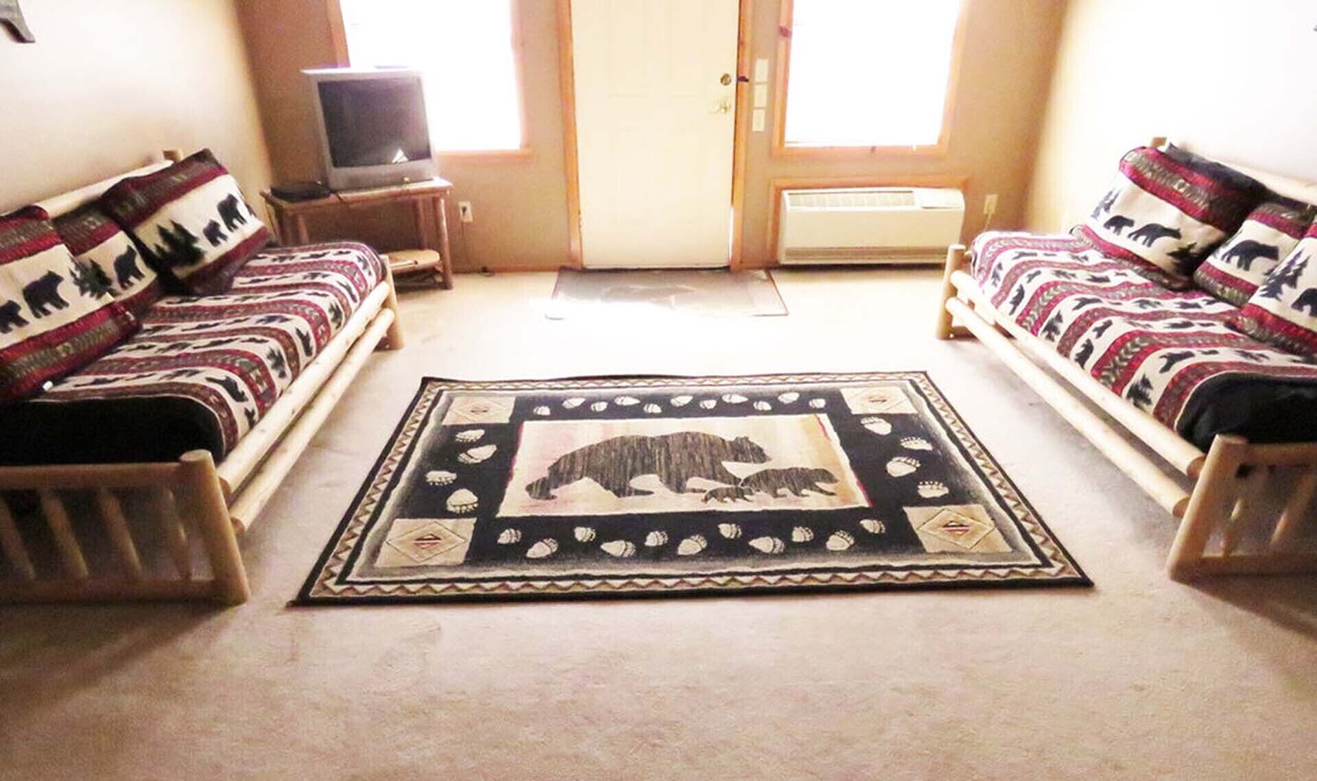 Ein Wohnzimmer mit zwei Sofas, einem Fernseher auf einem Schrank und einem Teppich mit Bärenmotiv.