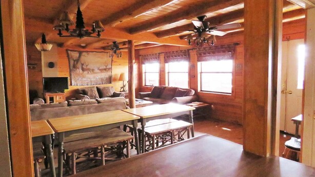 A rustic cabin interior with a wooden dining table, benches, a sofa, and a ceiling fan.