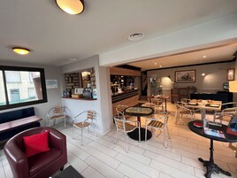 Un hall d’hôtel moderne doté d’un bar, de différents espaces pour s’asseoir et offrant une vue sur la rue.