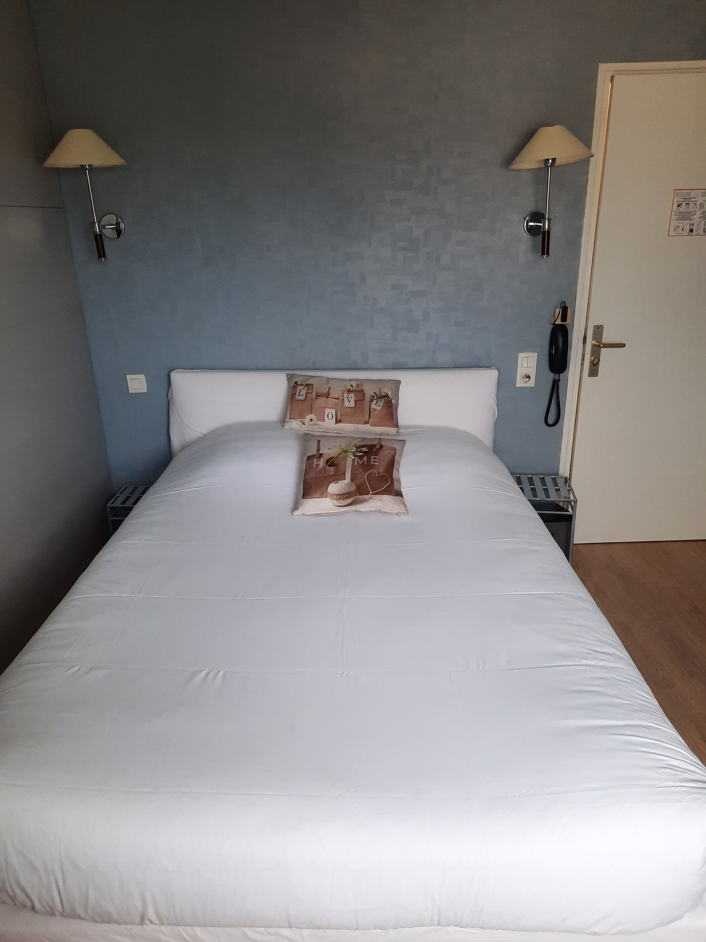 A neatly made bed with white linens, two wall-mounted lamps, and two decorative pillows with text and images.
