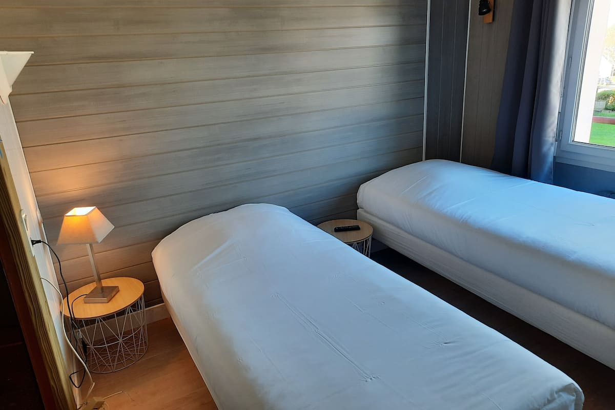 A hotel room with two single beds, a small round table with a lamp, and a window with curtains.