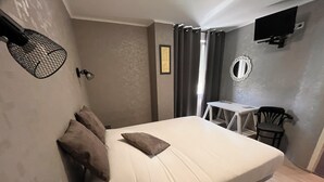 A bedroom with a bed, a desk, a chair, a TV, and a mirror. - Hôtel des Iles (Theix-Noyalo)