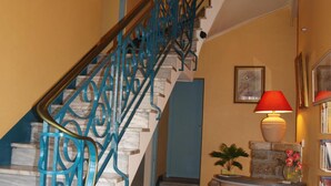 A staircase with blue railings, a white sofa with an orange pillow, a red lamp, and a bookshelf. - Hôtel des Iles (Theix-Noyalo)