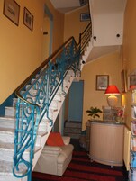 Un escalier avec des rampes bleues, un canapé blanc avec un coussin orange, une lampe rouge et une bibliothèque.