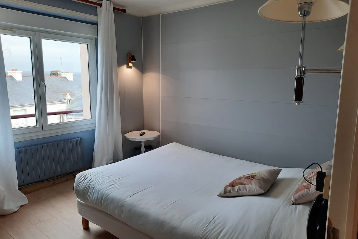 A bedroom with a bed, a bedside table, a lamp, and a window with curtains.