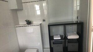A modern bathroom with a toilet, a shelf with folded towels, and a small potted plant. - Hôtel des Iles (Theix-Noyalo)