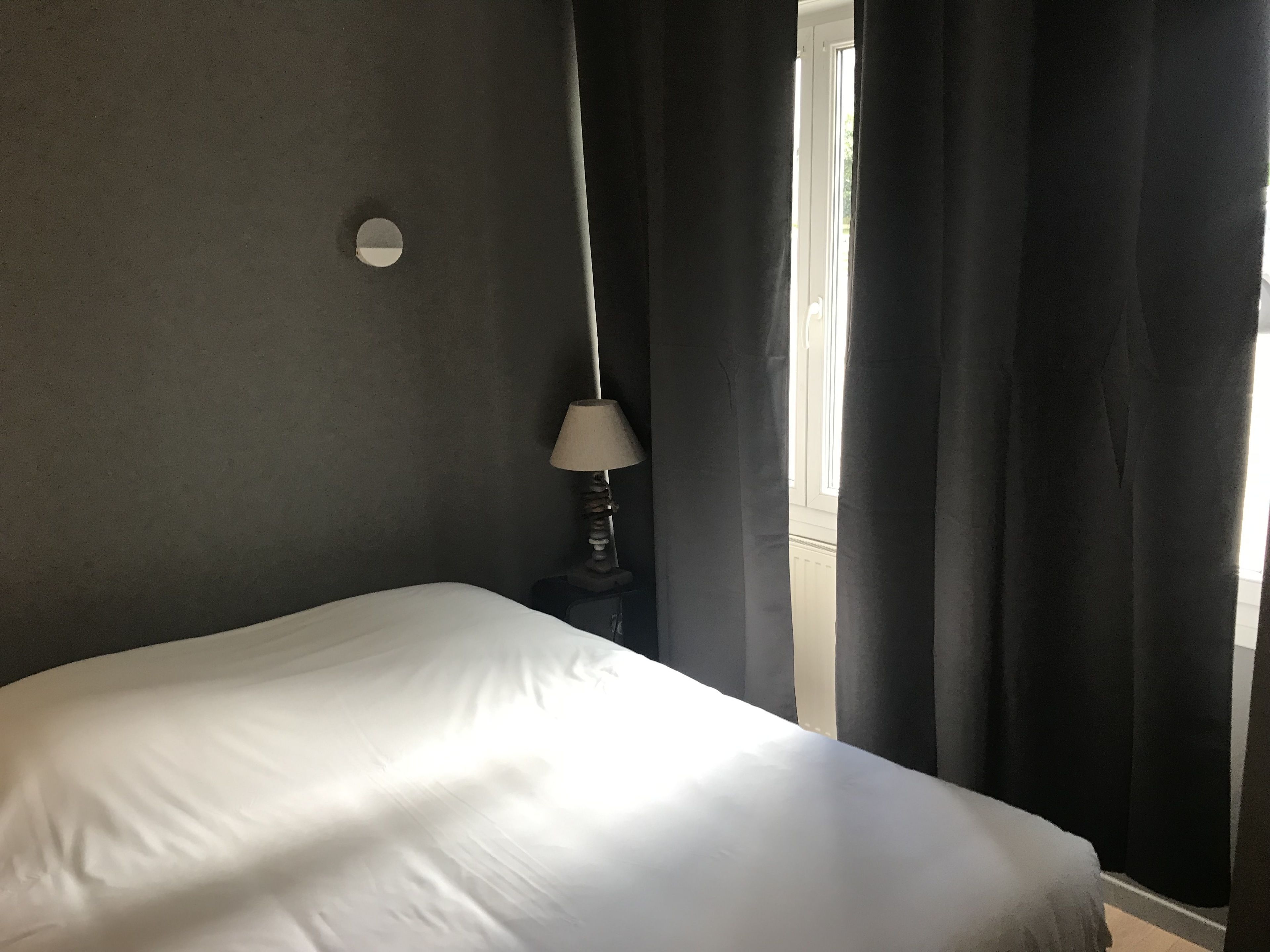 Een slaapkamer met een bed, een lamp en een raam met gordijnen.