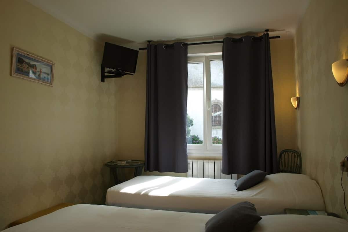A hotel room with two beds, a window with curtains, a small table, a chair, and a wall-mounted TV.