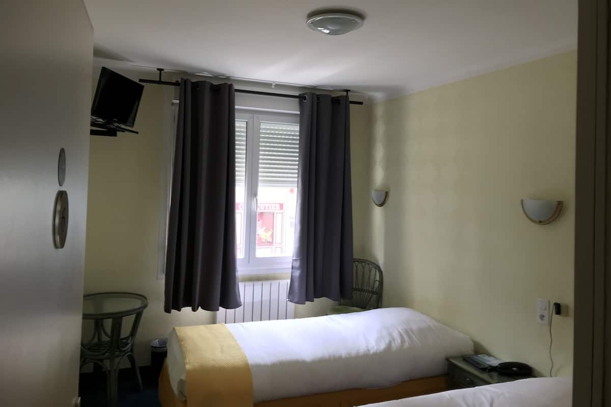 A small hotel room with a single bed, a chair, a table, a TV, and a window with curtains.