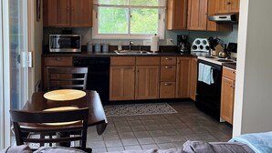 A compact kitchen with wooden cabinets, a microwave, a sink, and a stove. There's a dining table with chairs and a couch in the foreground. - Stowe 2 BR / 2 BA Vacation Condo off Mountain Road (Stowe)