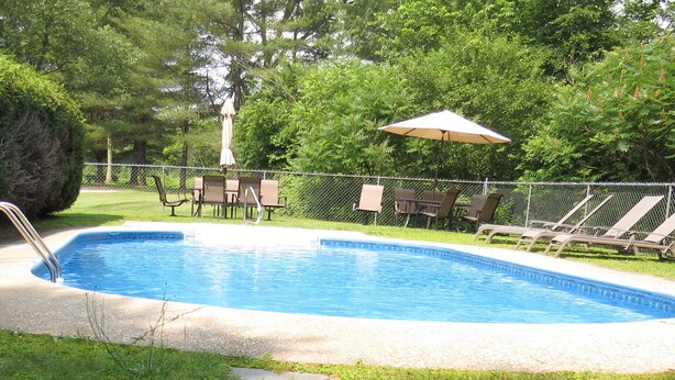 A rectangular swimming pool with a metal fence, surrounded by grass and trees. - Stowe 2 BR / 2 BA Vacation Condo off Mountain Road (Stowe)