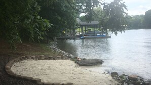 Un parque junto al lago con una zona de arena, un borde de piedra y un pabellón.