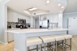 Uma cozinha moderna com armários brancos, uma ilha grande com banquetas, eletrodomésticos de aço inoxidável e um claraboia.