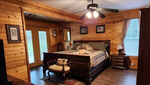 Un dormitorio con paneles de madera, una cama, una silla, una mesita de noche y un ventilador de techo.