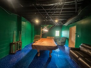 A room with a pool table, green walls, a blue speckled floor, a staircase, and a door. - Pines Lodge at Sand Run Lake WNF, Hocking Hills (Nelsonville)