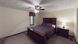 Un dormitorio con cama, mesita de noche, lámpara, ventilador de techo y ventana con cortinas.