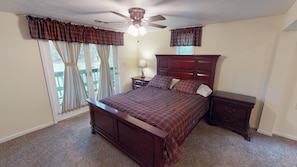 A bedroom with a wooden bed, a nightstand, a ceiling fan, and a window with curtains. - Pines Lodge at Sand Run Lake in WNF, Hocking Hills (Nelsonville)