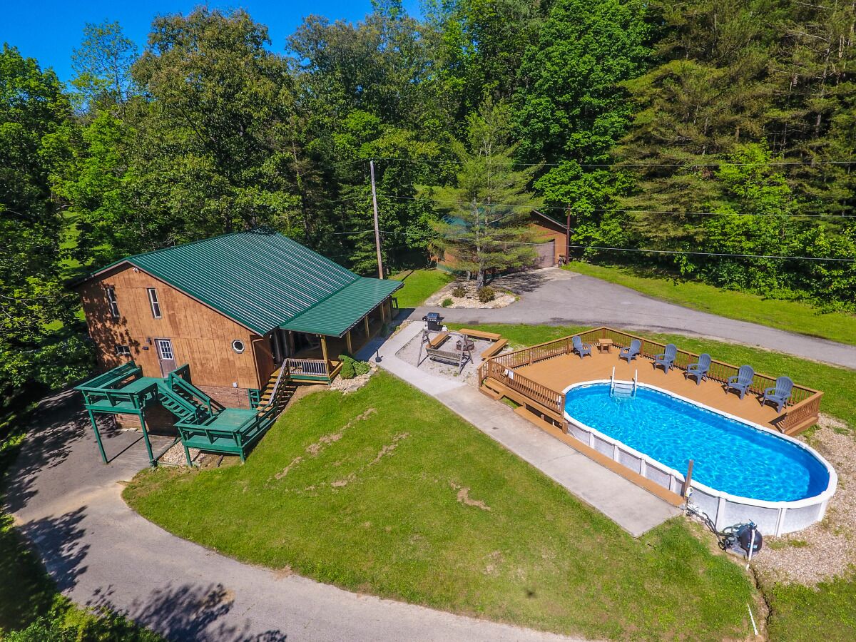 A wooden cabin with a green roof, a swimming pool, and a deck with chairs.
