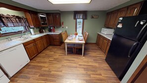 A compact kitchen with wooden cabinets, a dining table set for four, a refrigerator, and a microwave. - Pines Lodge at Sand Run Lake in WNF, Hocking Hills (Nelsonville)