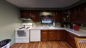 A compact kitchen with wooden cabinets, a white stove, a dishwasher, and a granite countertop. - Pines Lodge at Sand Run Lake WNF, Hocking Hills (Nelsonville)