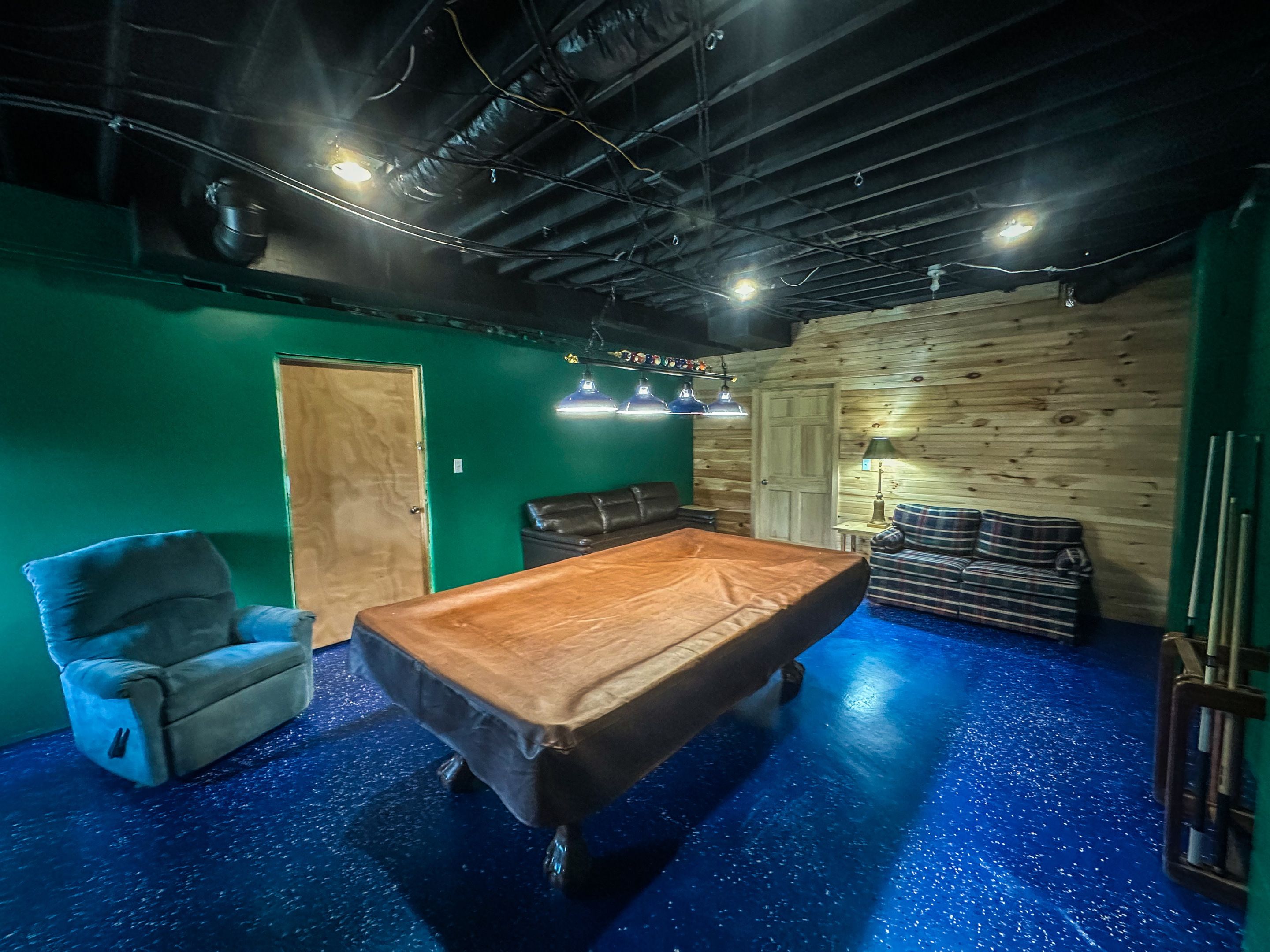Una sala de billar con mesa de pool, pared verde y pared de madera.