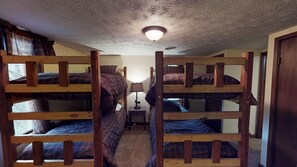 A dormitory room with bunk beds, a small bedside table with a lamp, and a ceiling light fixture.