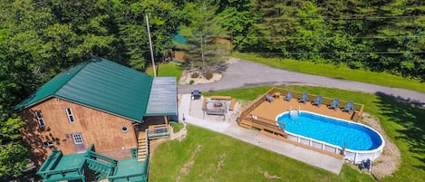 Un edificio de dos pisos con techo verde, piscina y terraza con sillas.