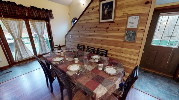 A dining area with a wooden table set for four, chairs, and a view of the outdoors through a window. - Pines Lodge at Sand Run Lake in WNF, Hocking Hills (Nelsonville)